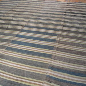 Flatweave striped rug in muted blue, gray, tan, and cream on a light brown wooden floor.
