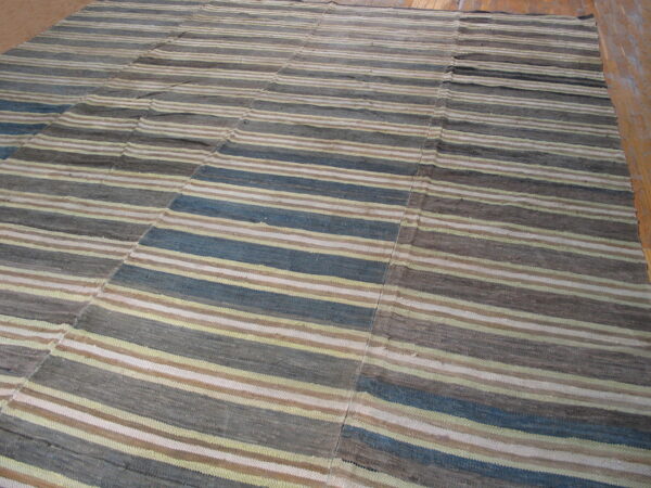 Flatweave striped rug in muted blue, gray, tan, and cream on a light brown wooden floor.