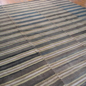 Flatweave rug with seams features varied horizontal stripes in gray, brown, cream, and hints of blue on wood flooring.