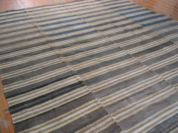 Flatweave rug with seams features varied horizontal stripes in gray, brown, cream, and hints of blue on wood flooring.