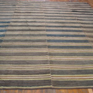 Flatweave rug with horizontal stripes of brown, gray, blue, and beige on wood flooring.
