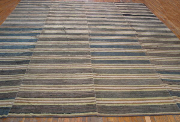 Flatweave rug with horizontal stripes of brown, gray, blue, and beige on wood flooring.