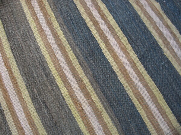 Diagonal striped rug in a coarse flat weave showing blue, gray, yellow, brown, and light beige colors.