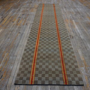 Tan and brown checkerboard runner with twin vertical red and yellow stripes rests on worn hardwood flooring.