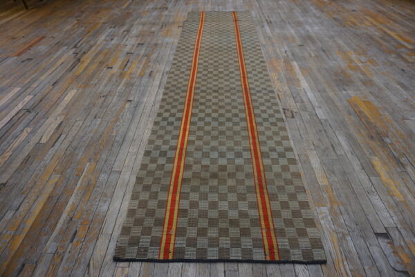 Tan and brown checkerboard runner with twin vertical red and yellow stripes rests on worn hardwood flooring.