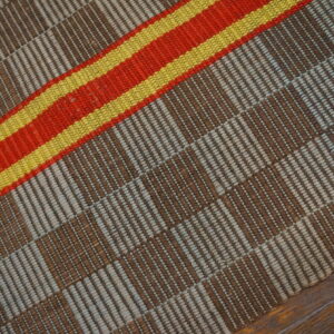 Structured brown and beige rug with a diagonal band of bright red and yellow stripes rests on wood flooring.