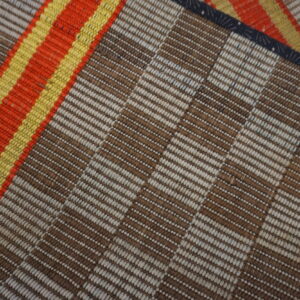 The flatwoven rug features alternating brown and beige stripes next to bright orange and yellow bands.