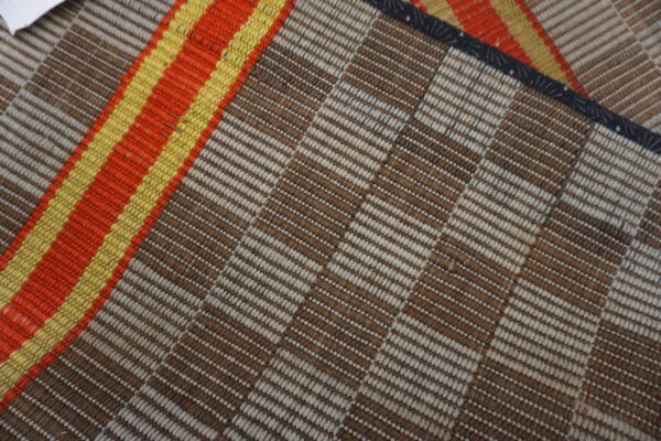 The flatwoven rug features alternating brown and beige stripes next to bright orange and yellow bands.