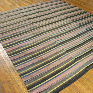 Irregular striped rug in yellow, blue, pink, and black colors rests on distressed hardwood floors.
