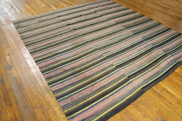 Irregular striped rug in yellow, blue, pink, and black colors rests on distressed hardwood floors.