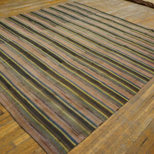 A flatweave rug with dark, yellow, pink, and blue stripes rests on worn wooden planks.