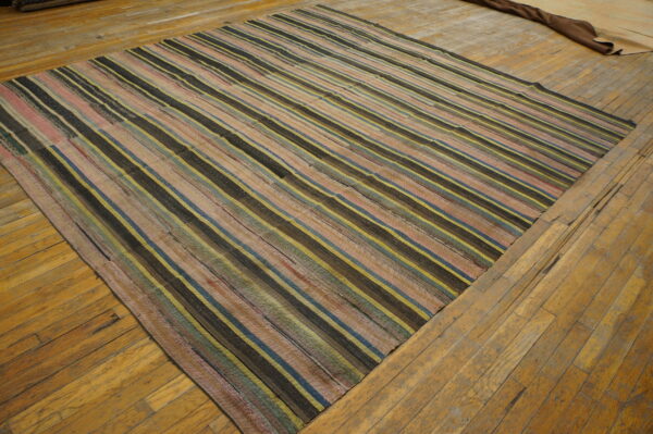 A flatweave rug with dark, yellow, pink, and blue stripes rests on worn wooden planks.
