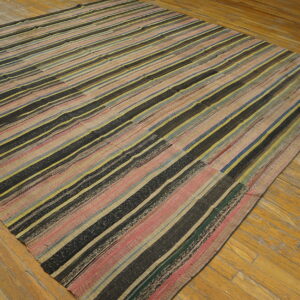 Low-pile rug with black, pink, yellow, and blue vertical stripes covers a distressed wood floor.