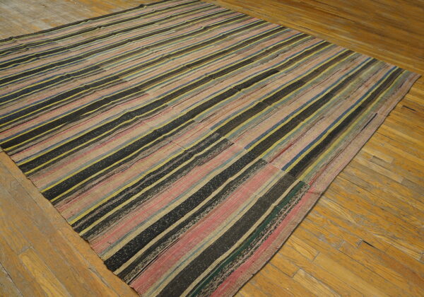 Low-pile rug with black, pink, yellow, and blue vertical stripes covers a distressed wood floor.
