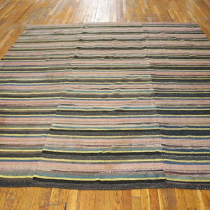 Multicolored striped rug featuring pink, yellow, blue, and black stripes, constructed from joined panels on a hardwood floor.