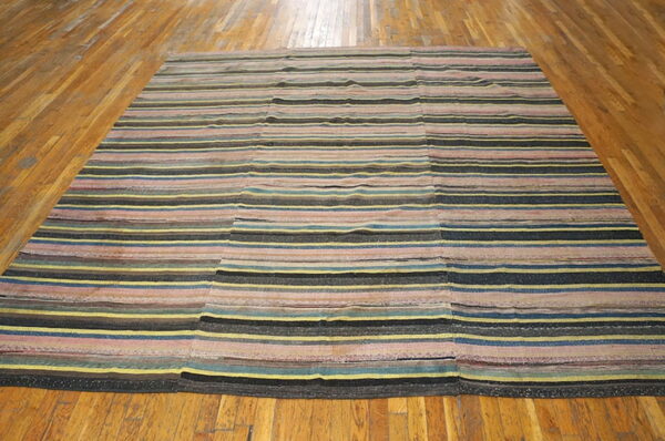 Multicolored striped rug featuring pink, yellow, blue, and black stripes, constructed from joined panels on a hardwood floor.