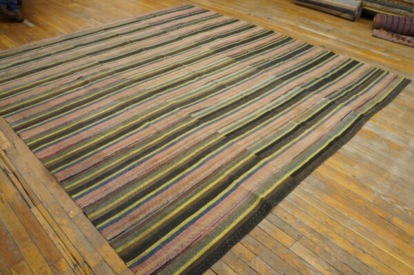 Highly textured, multicolored striped flatweave rug displayed on glossy, aged wood plank flooring.