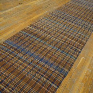 Narrow flatweave American Rag Rug runner showing blue, orange, and brown plaid stripes on distressed wood flooring.