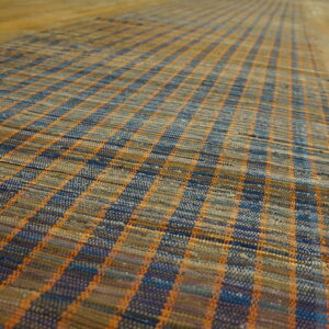 Flatwoven American Rag Rug runner in mixed blue, tan, and orange plaid texture on wide plank wood flooring.