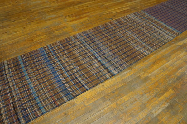 Vintage american rag rug hallway runner multicolor 1950s 6 A brown and blue plaid american rag rug runner with a dark striped end rests on a worn wood floor.