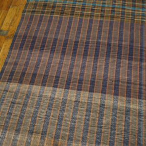 A flatweave runner rug with thin vertical stripes in navy, orange, and gray rests on a wooden floor.