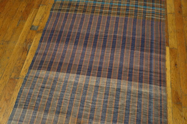 Vintage american rag rug hallway runner multicolor 1950s 8 A flatweave runner rug with thin vertical stripes in navy, orange, and gray rests on a wooden floor.