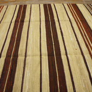 Flatweave rug displaying vertical wide stripes of light tan and narrower stripes of brown and rust on a wood floor.