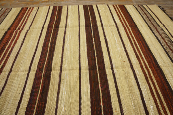 Flatweave rug displaying vertical wide stripes of light tan and narrower stripes of brown and rust on a wood floor.