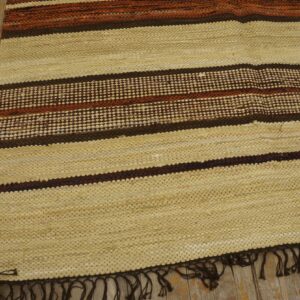 Textured cream rug with horizontal dark brown and orange stripes rests on distressed wood flooring.