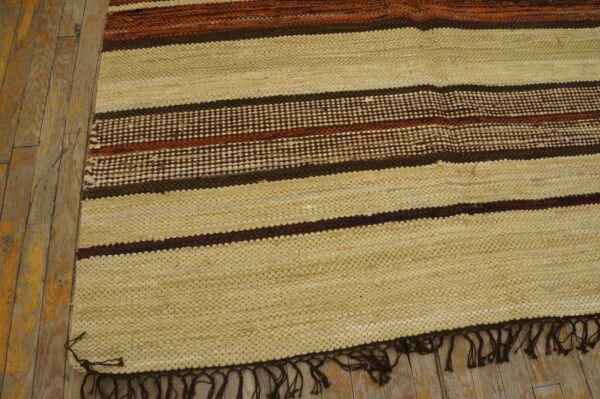 Textured cream rug with horizontal dark brown and orange stripes rests on distressed wood flooring.