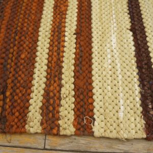 Cream, rust, and dark brown looped rug with bold vertical stripes resting on distressed wooden planks.