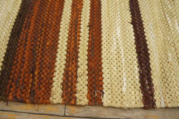 Cream, rust, and dark brown looped rug with bold vertical stripes resting on distressed wooden planks.