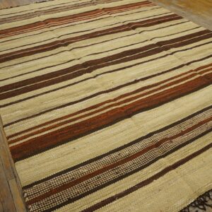 Textured flatweave rug in beige, dark brown, and reddish stripes rests on distressed wood flooring.