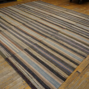 Multi-colored striped flatweave rug assembled from patched panels lying on rustic wood planks.