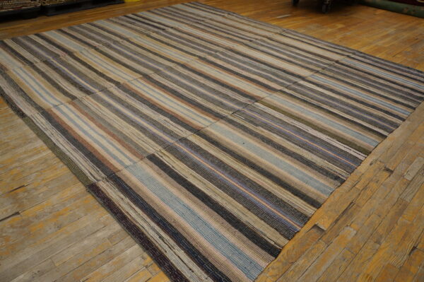 Multi-colored striped flatweave rug assembled from patched panels lying on rustic wood planks.