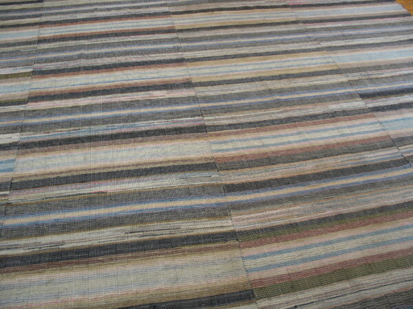 A low-profile rug with multi-colored horizontal stripes in shades of gray, blue, tan, and rust.