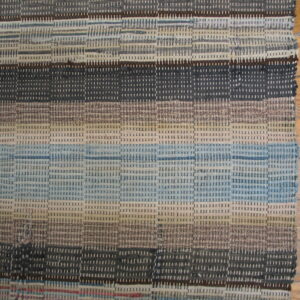 Textured flatweave rug with horizontal stripes in gray, blue, and brown covers a natural hardwood floor.