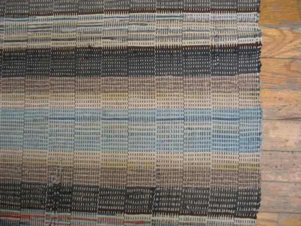 Textured flatweave rug with horizontal stripes in gray, blue, and brown covers a natural hardwood floor.
