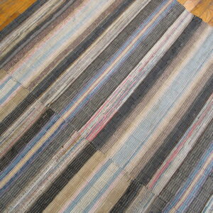 Textured rag rug with vertical stripes in tan, blue, dark gray, and red on wood flooring.