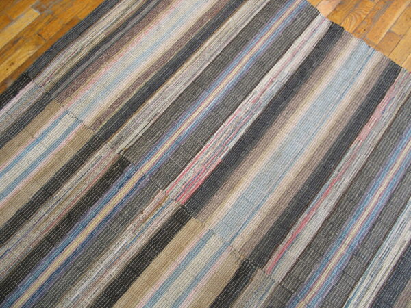 Textured rag rug with vertical stripes in tan, blue, dark gray, and red on wood flooring.
