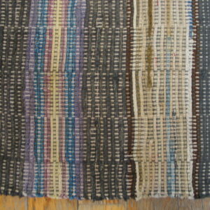 Multicolor rag flatweave rug with vertical stripes of gray, blue, purple, and cream rests on wood flooring.
