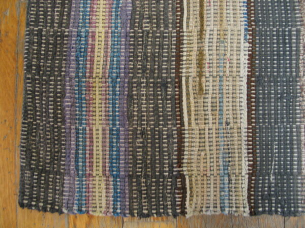 Multicolor rag flatweave rug with vertical stripes of gray, blue, purple, and cream rests on wood flooring.