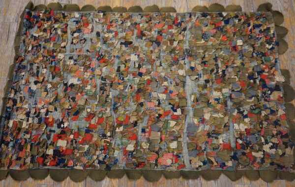 Highly textured rag rug composed of colorful fabric patches and framed by a dark olive scalloped border.