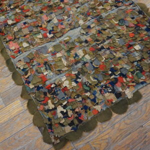 Shaggy patchwork rug featuring colorful scraps and an olive green scalloped trim on light wood flooring.
