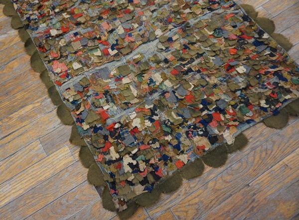Shaggy patchwork rug featuring colorful scraps and an olive green scalloped trim on light wood flooring.