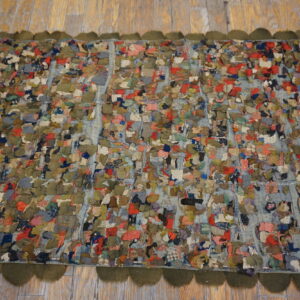 A multicolored scrap rag rug with a high texture and scalloped olive border rests on light wood floors.