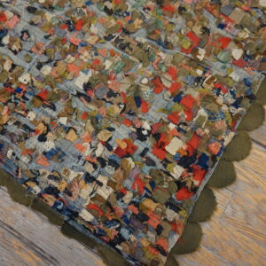 Multicolored fabric scraps create a textured rag rug with an olive scalloped edge on light wood floorboards.