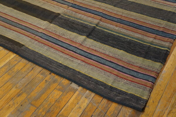 A multicolored, low-pile flatweave rug with horizontal stripes rests on distressed yellow wood floorboards.