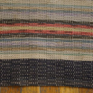 Chunky textured rug featuring multicolored horizontal stripes of cream, red, blue, and dark gray over wood flooring.