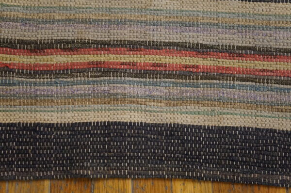 Chunky textured rug featuring multicolored horizontal stripes of cream, red, blue, and dark gray over wood flooring.